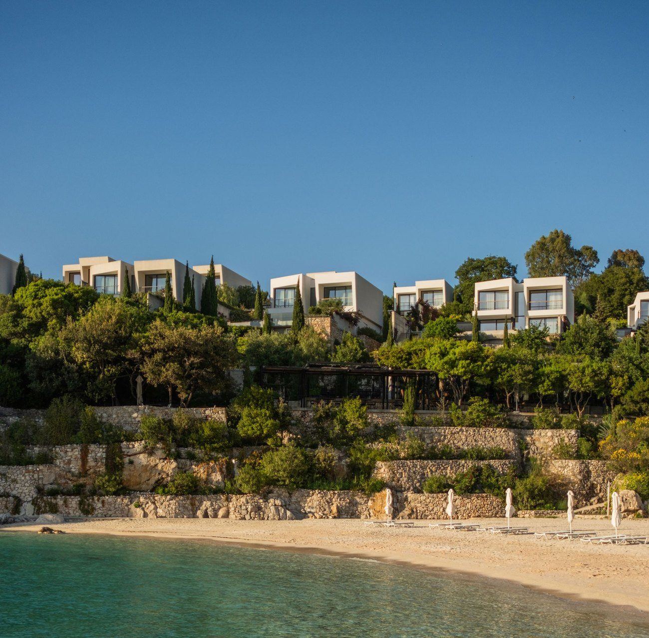 White villas among trees above a small sandy beach