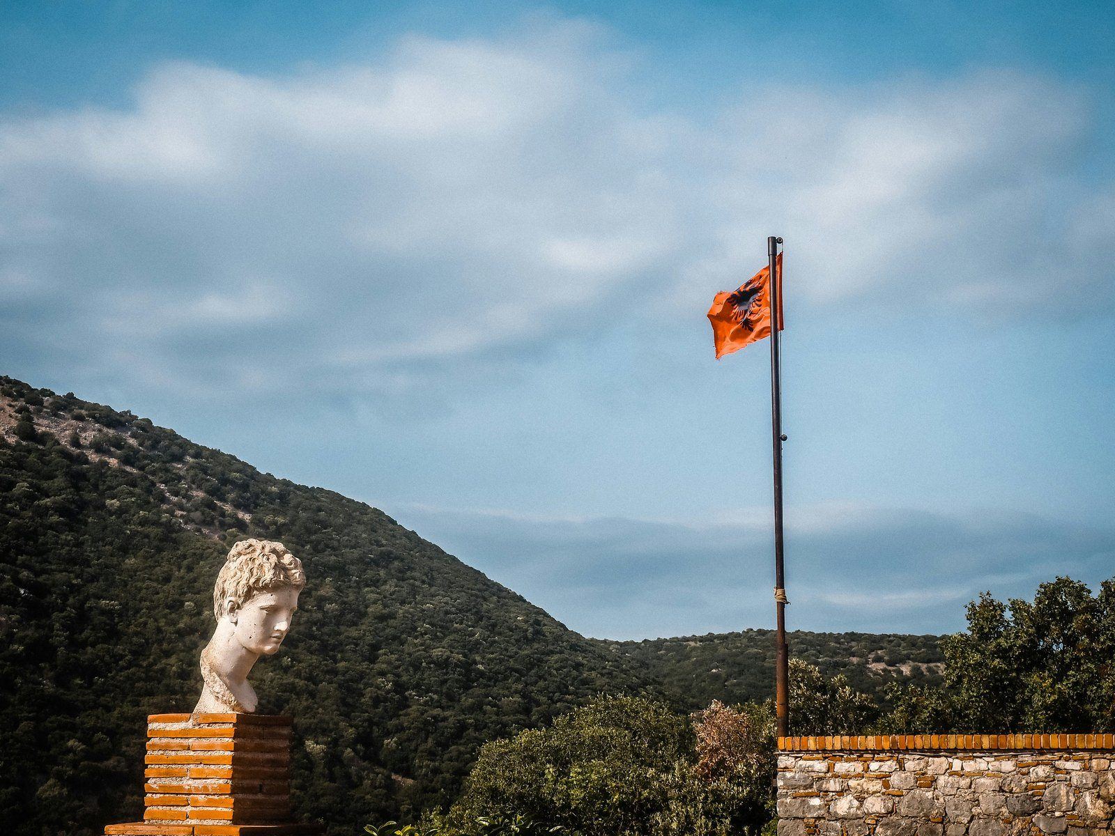 Antique marble bust and the Albanian flag against green hills and sky